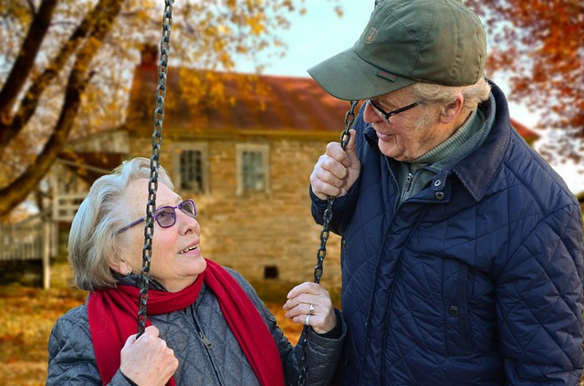 A mature couple sitting on a swingset.